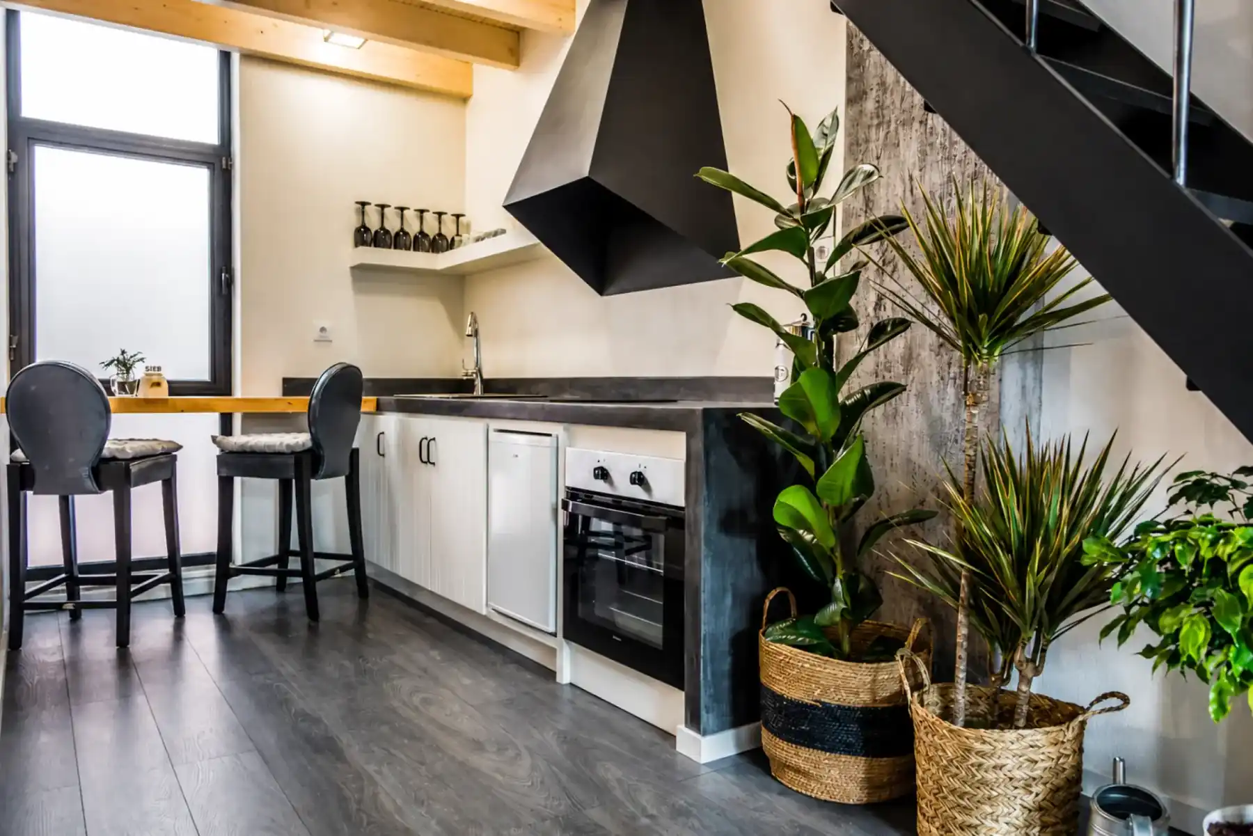 Modern kitchen with oven, hob, breakfast bar and stools beside a window