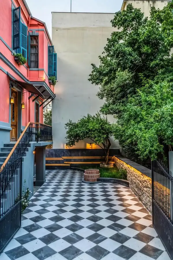 Chequered courtyard patio with benches, a small tree and lanterns lit at dusk