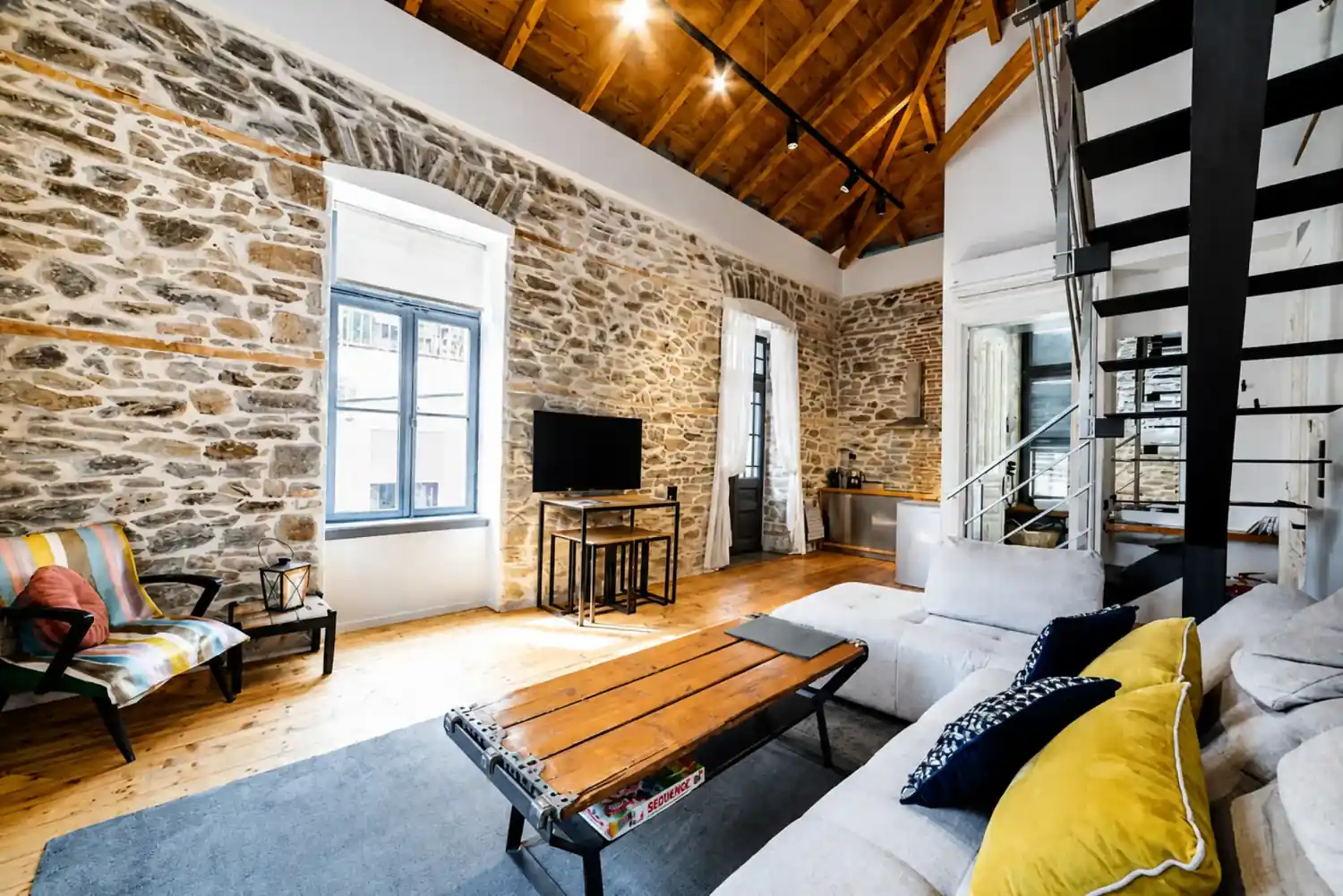 Living area with exposed stone walls, a beamed timber ceiling and tall windows